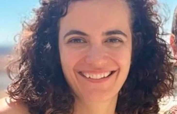 Smiling woman with dark curly hair in a close-up outdoors against a light blue sky