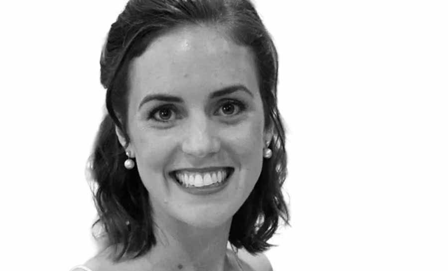 Black-and-white portrait of a smiling woman with shoulder-length wavy hair and pearl earrings against a light background