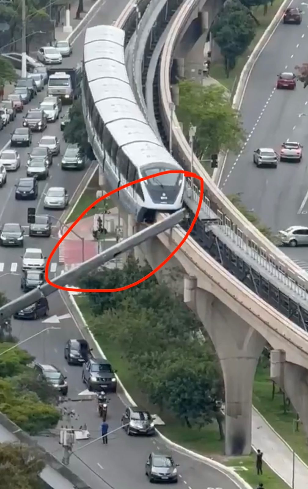 Monorotaia su viadotto sopraelevato: davanti al treno un braccio di gru caduto sporge in diagonale su una strada con auto; evidenziato in rosso.