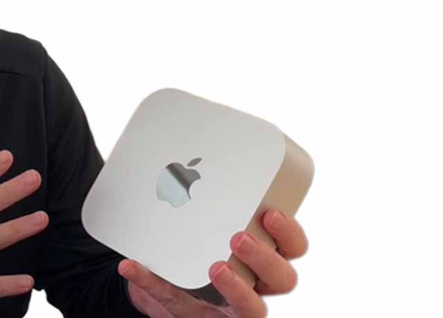 Una persona con una prenda oscura sostiene un pequeño ordenador plateado con el logotipo de Apple frente a un fondo blanco.